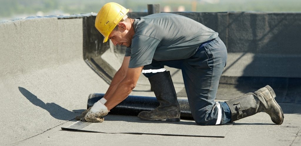 a worker installing a roll of waterproofing membrane on a flat roof